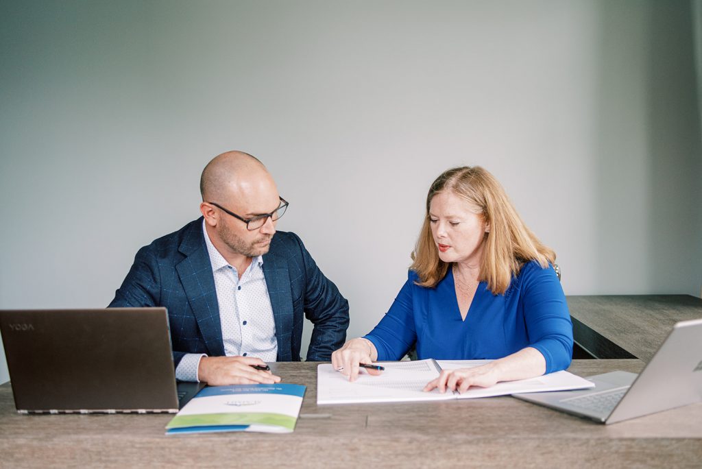 Two people sit at a desk, studying a book between them